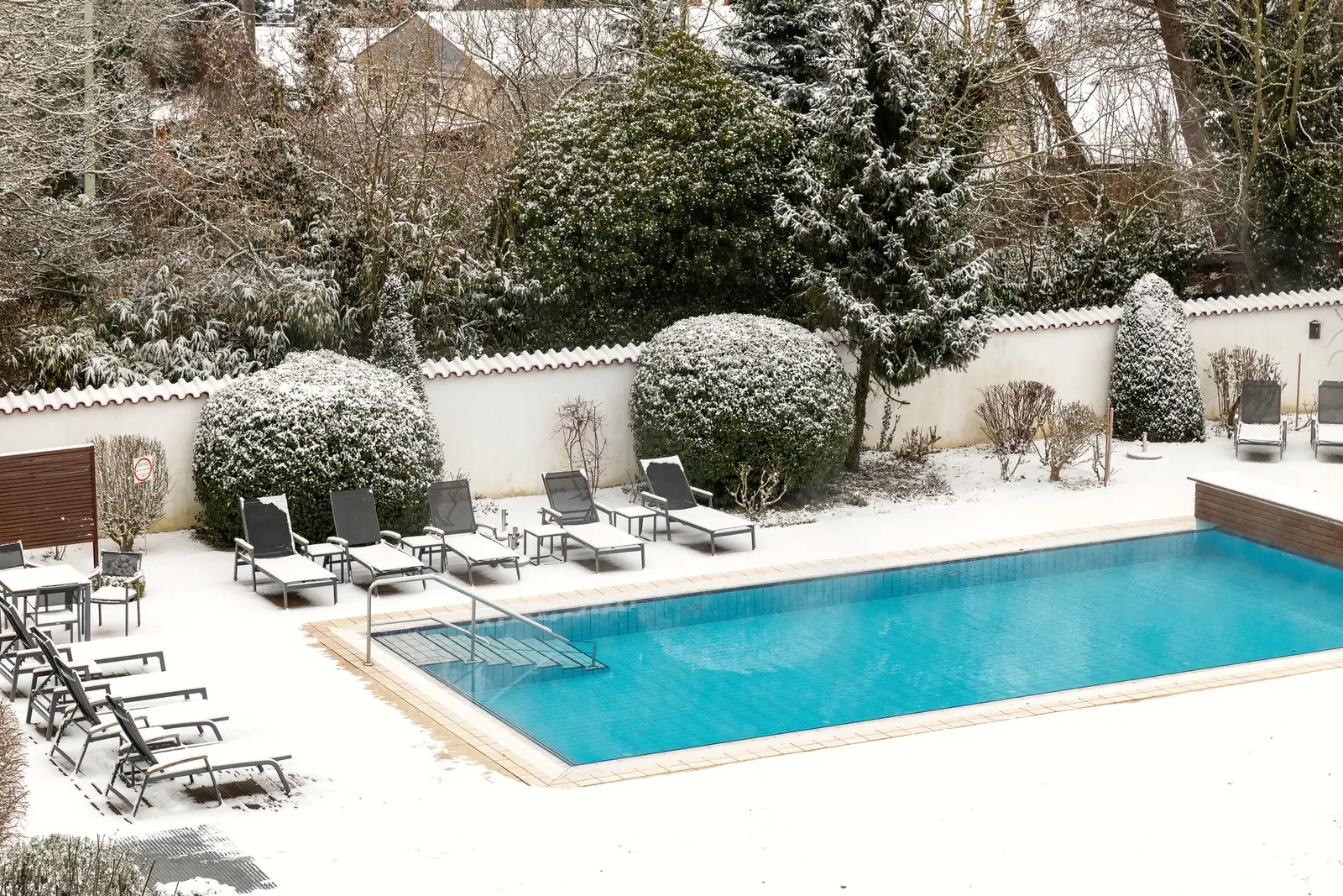 Blick von oben auf den beheizten Außenpool im verschneiten Garten des Hotel Krone, Liegen und Hecke im Schnee