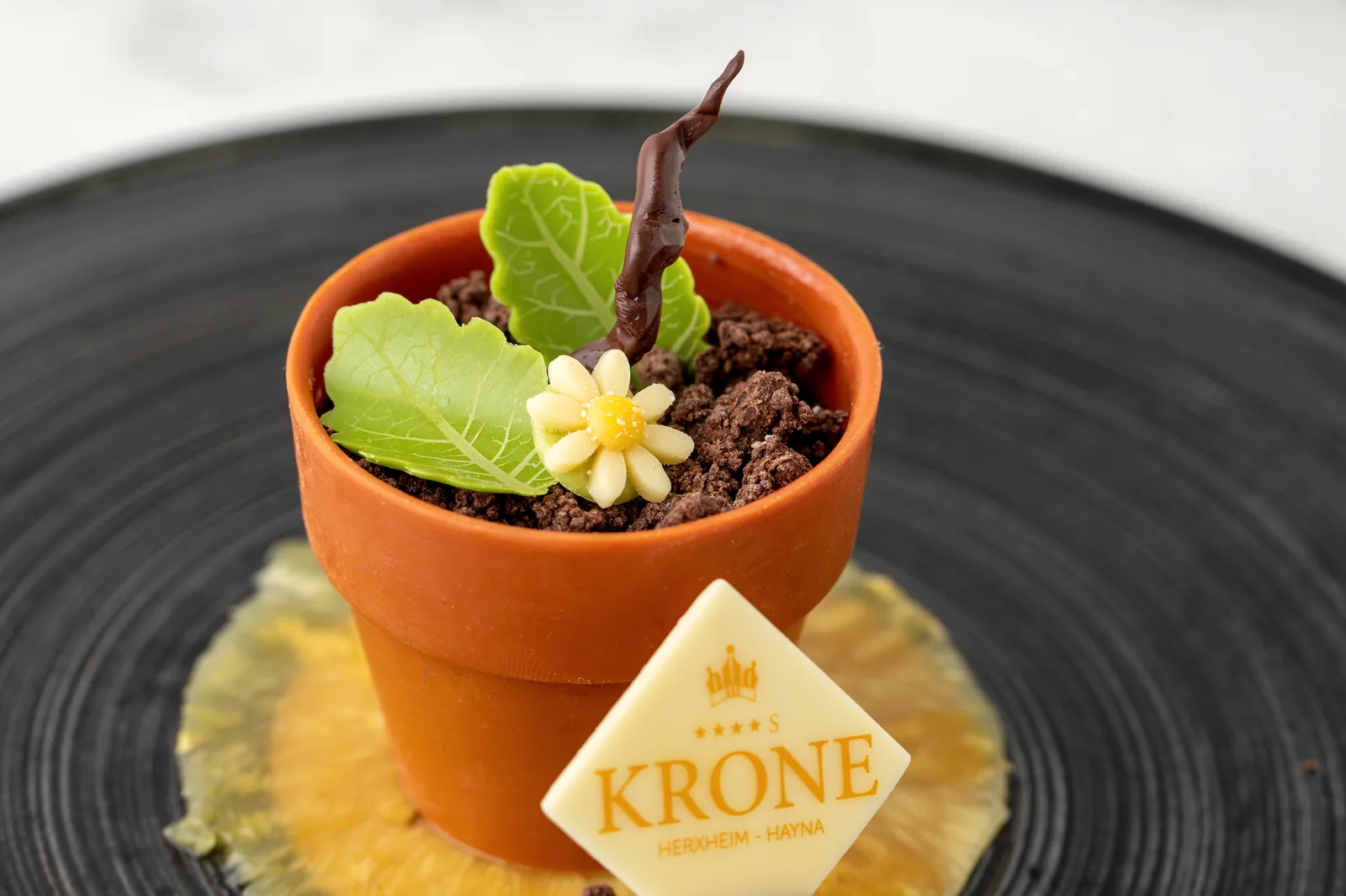 Dessert im kleinen Blumentopf mit Schokoladenerde, essbarer Blüte und Krone-Plakette