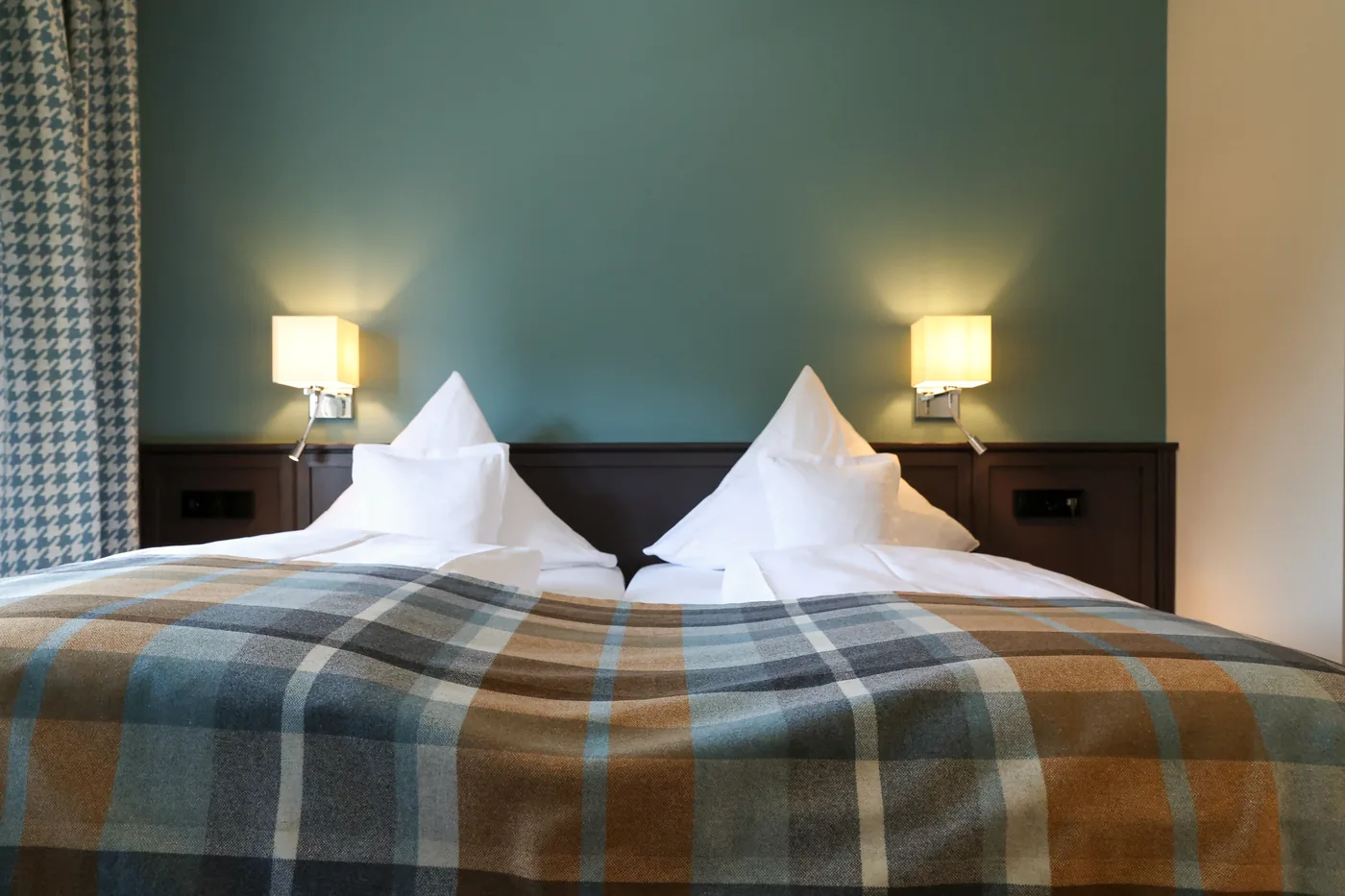 Doppelbett mit karierter Decke vor petrolfarbener Wand in einem 2025 renovierten Zimmer des Hotel Krone