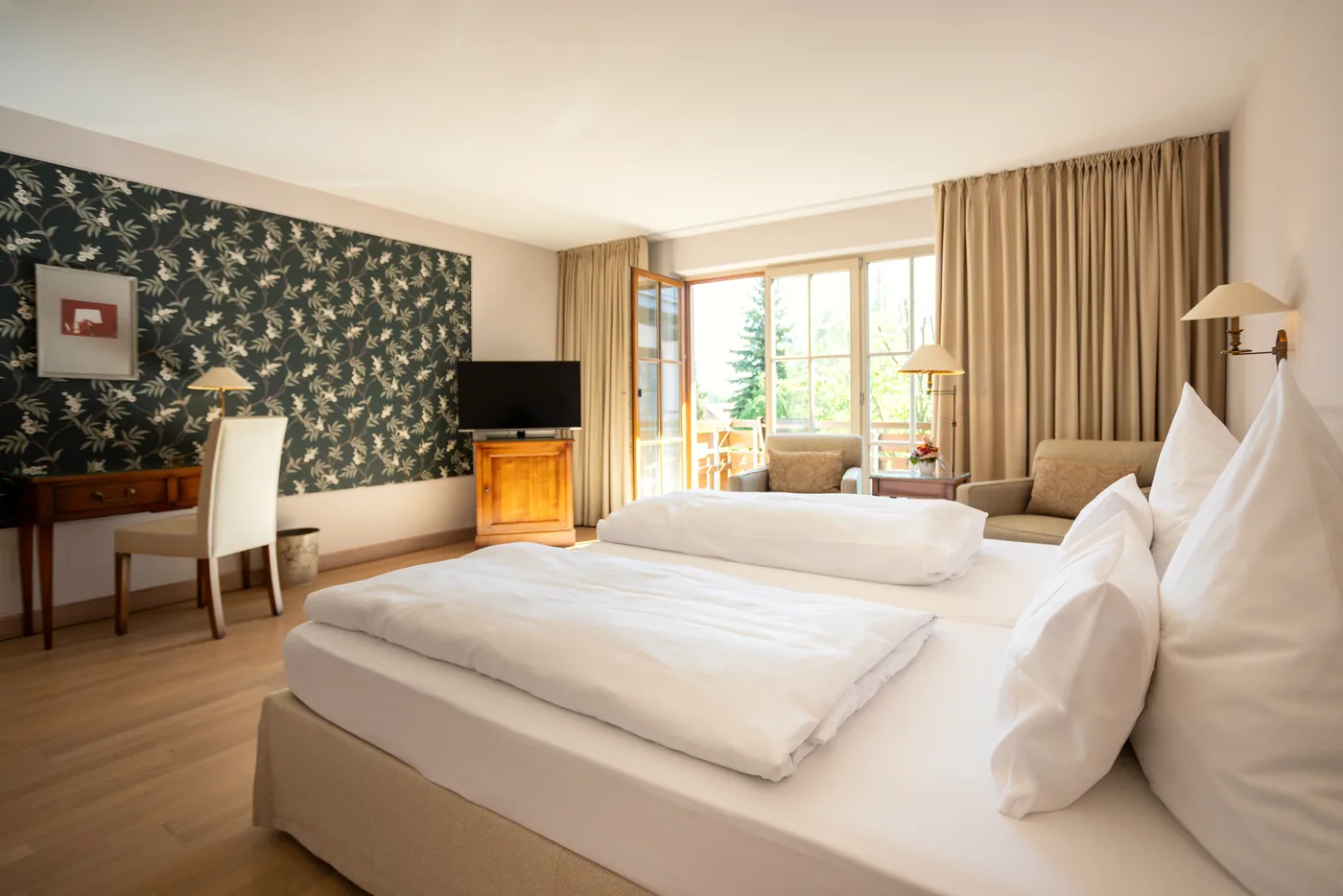 Helles Doppelzimmer mit grüner Blumentapete, Schreibtisch und Blick zum Balkon im Hotel Krone