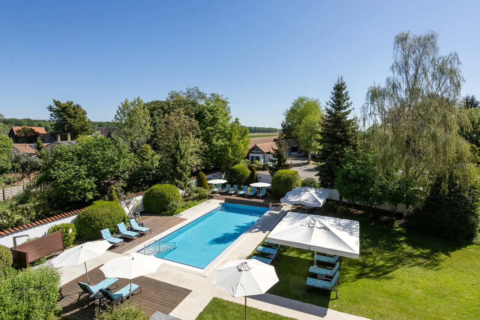 Luftaufnahme: der Garten des Hotel Krone mit Außenpool, Liegen, Sonnenschirmen und alten Bäumen