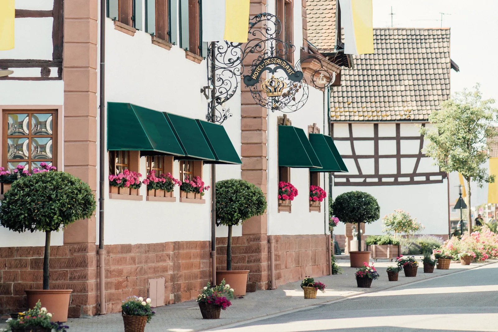 Fassade des Hotel Krone in Herxheim-Hayna von der Straße aus, mit grünen Markisen und schmiedeeisernem Wirtshausschild