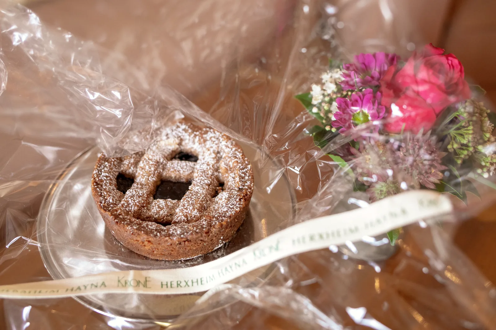 Kleine Linzer Torte in Cellophan mit Blumenstrauß als Willkommensgruß auf dem Zimmer