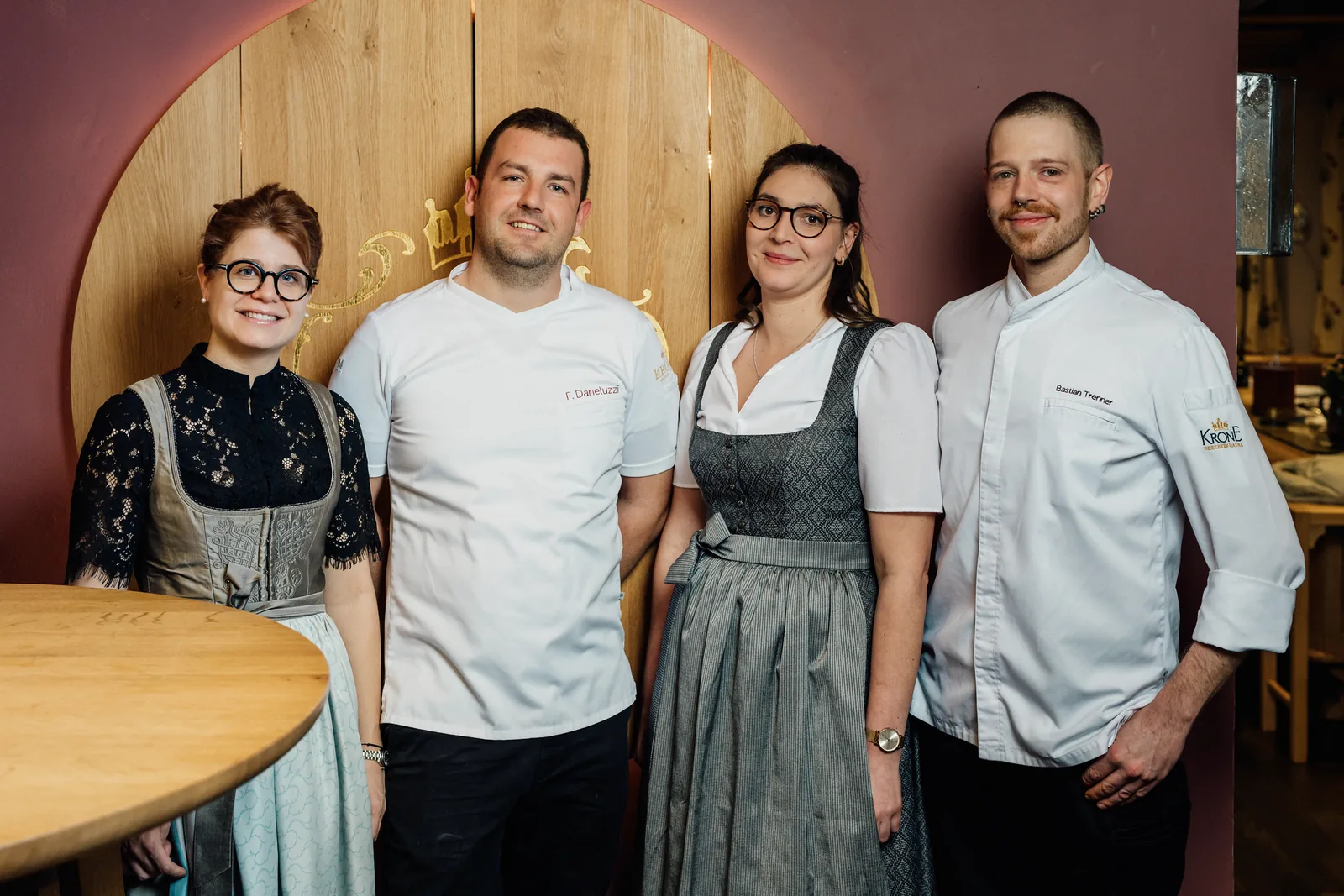 Drei Mitarbeitende aus Küche und Service des Hotel Krone vor einer weinroten Holzwand