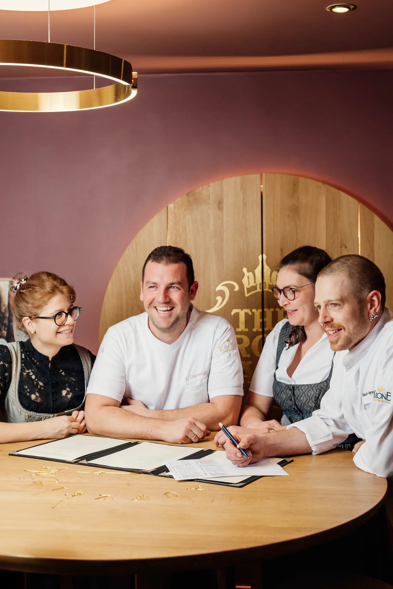 Köche und Servicekräfte des Hotel Krone besprechen die Speisekarte an einem runden Holztisch