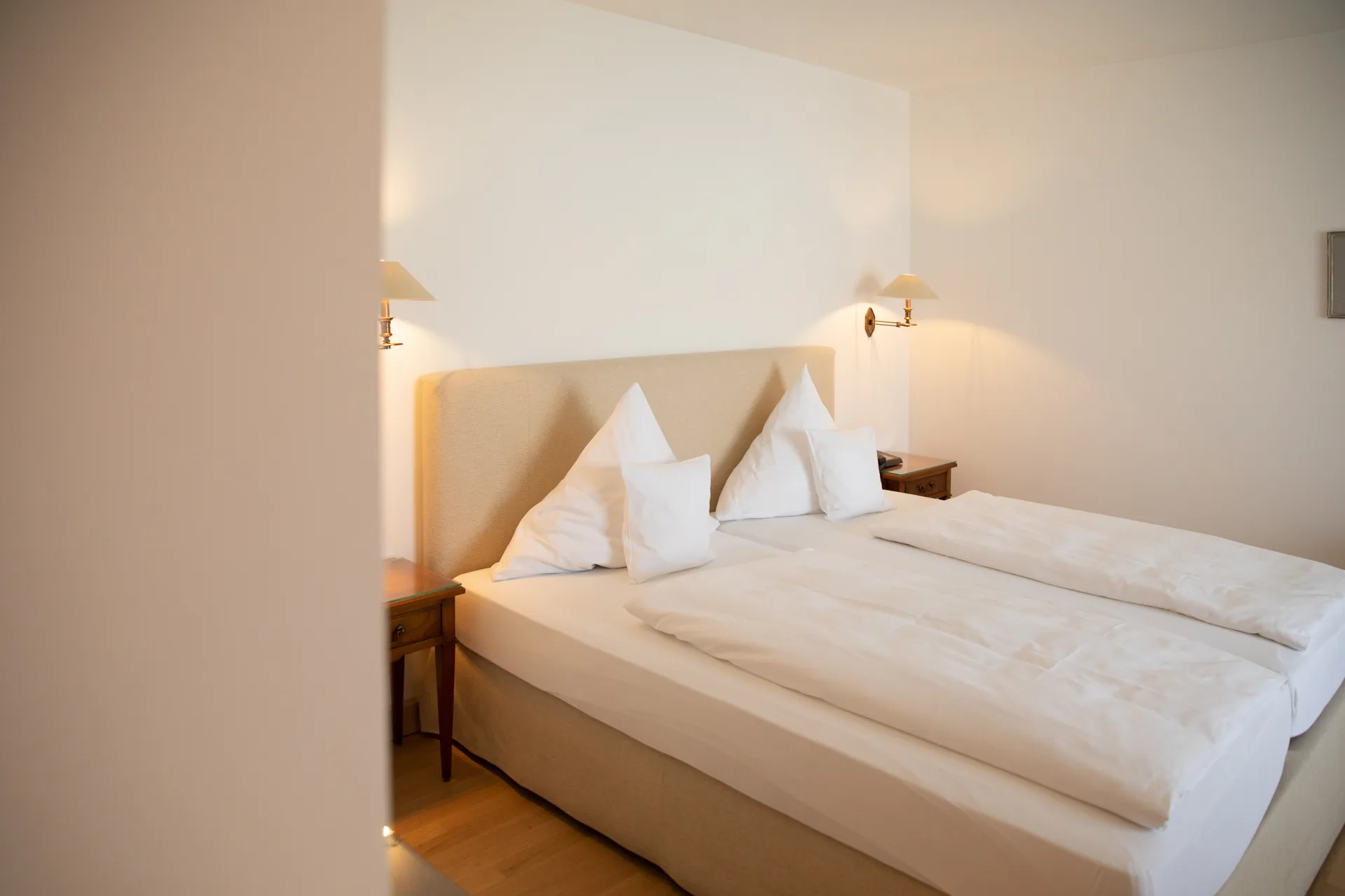 Doppelbett mit weißem Kopfteil und Wandleuchten im Doppelzimmer Basic des Hotel Krone