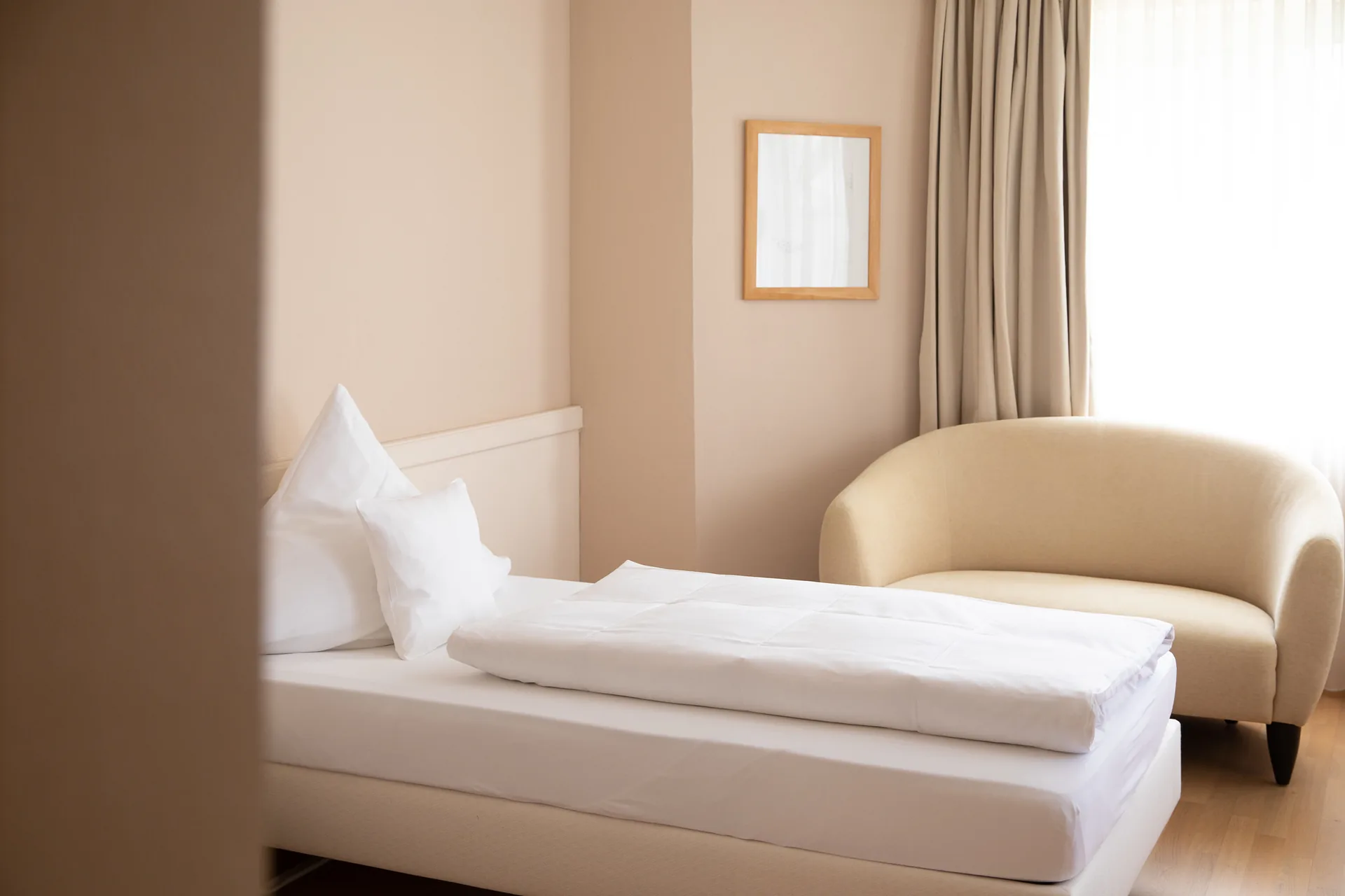 Einzelzimmer mit Bett, cremefarbenem Sessel und Bild an der Wand