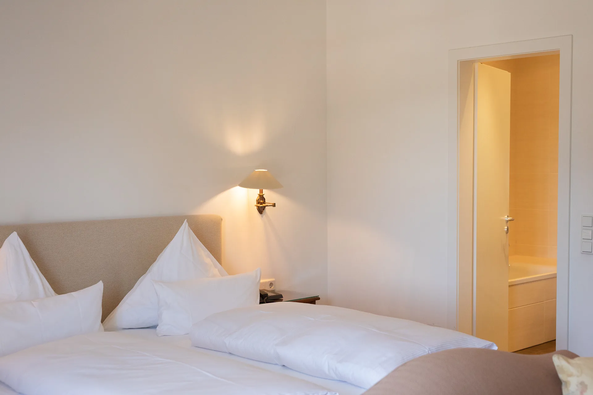 Helles Doppelzimmer Gold mit Boxspringbett, Wandleuchten und Blick zur offenen Tür
