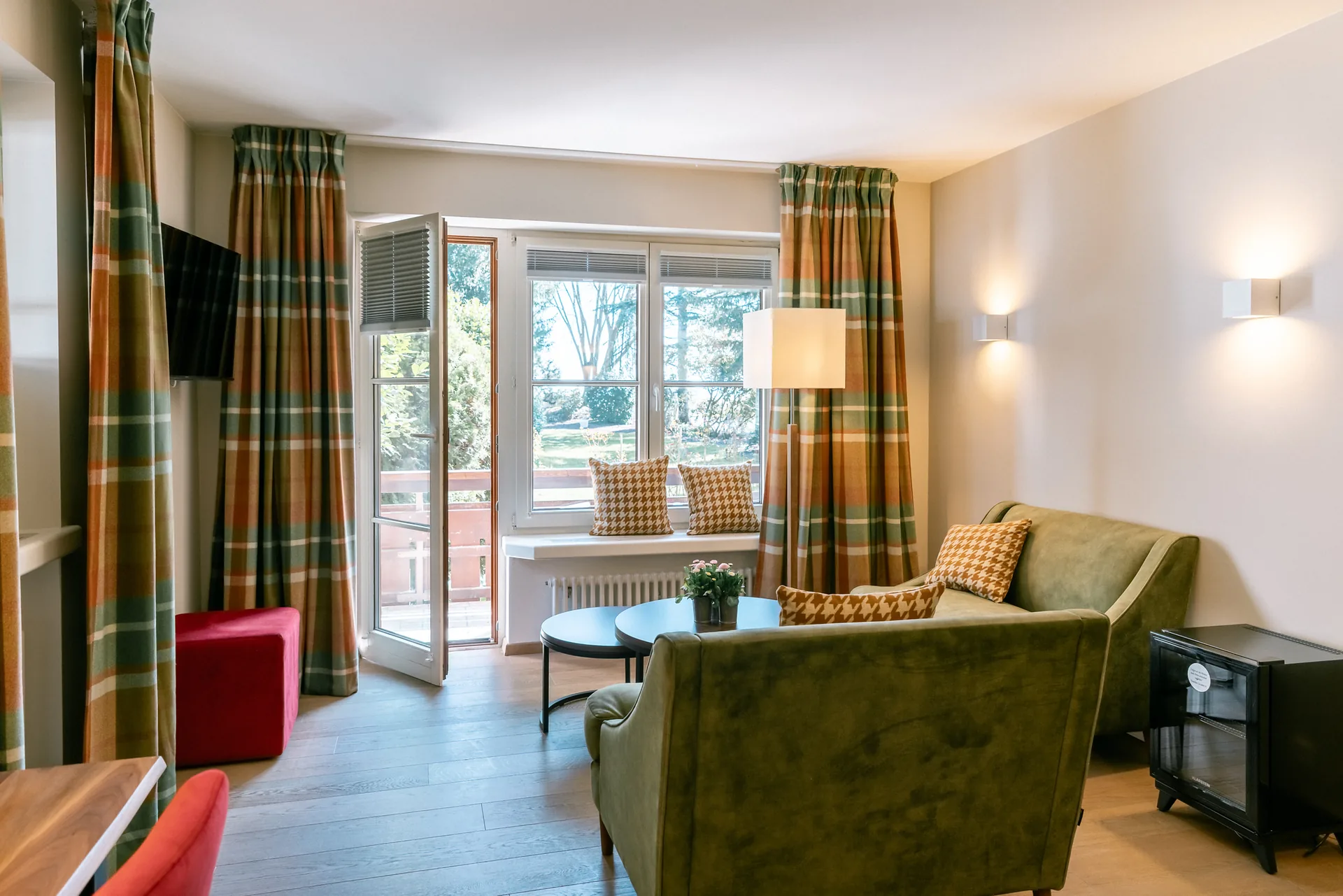 Junior Suite mit grünem Sofa, rotem Sessel und Fenstertür zum Balkon