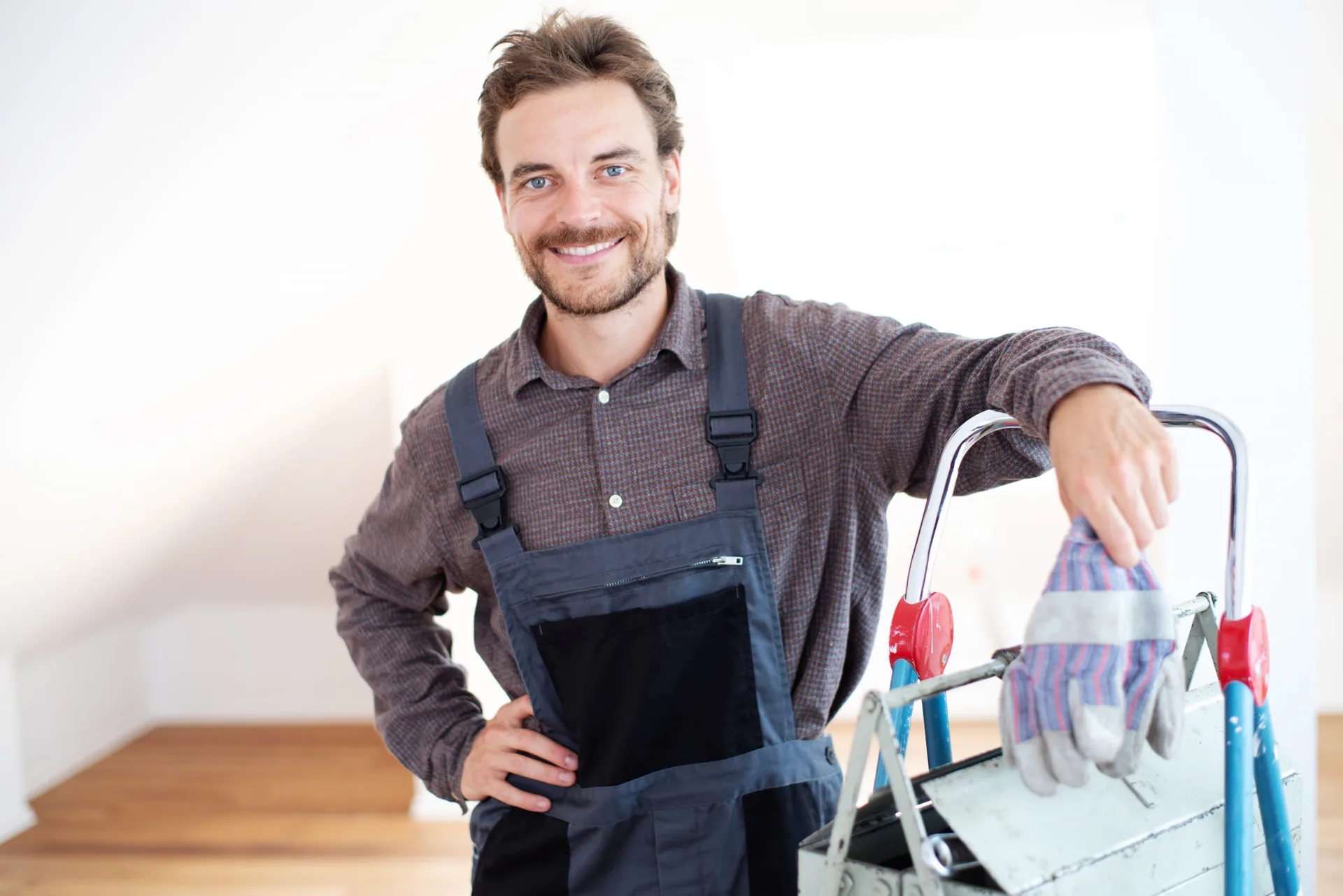 Haustechniker in Arbeitslatzhose stützt sich auf eine Leiter mit Werkzeug