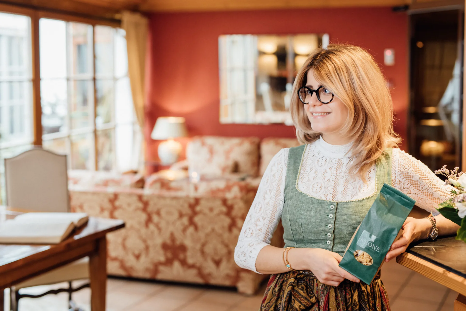 Mitarbeiterin im Dirndl mit einer Krone-Tüte in der gemütlichen Stube des Hotel Krone