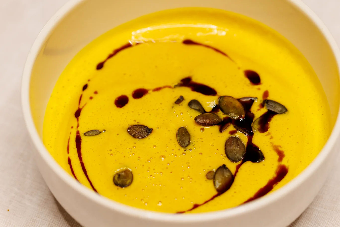 Kürbissuppe mit Kürbiskernöl und Kernen in weißer Schale