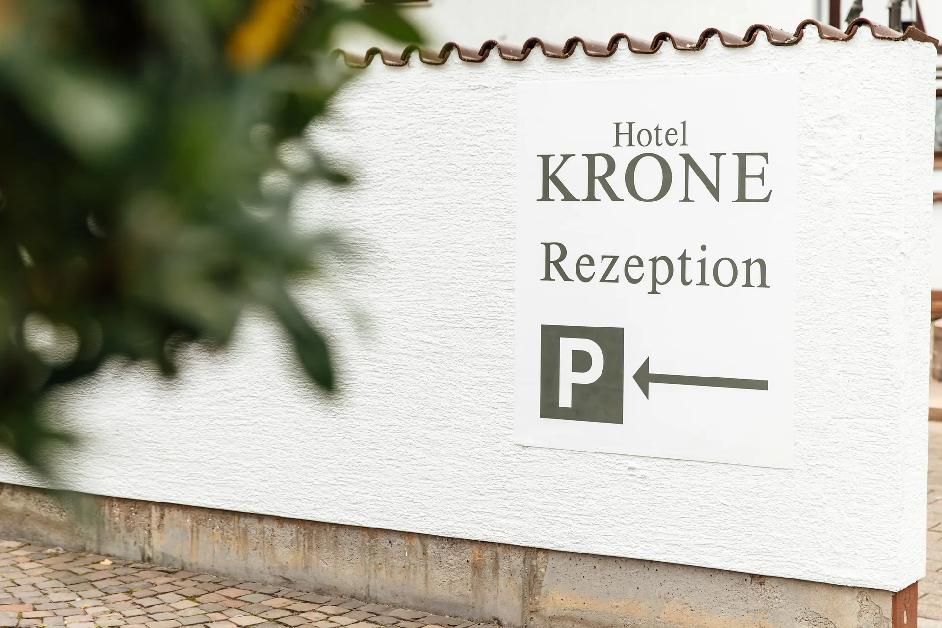 Schild Hotel Krone Rezeption mit Pfeil zum Parkplatz an der weißen Hauswand
