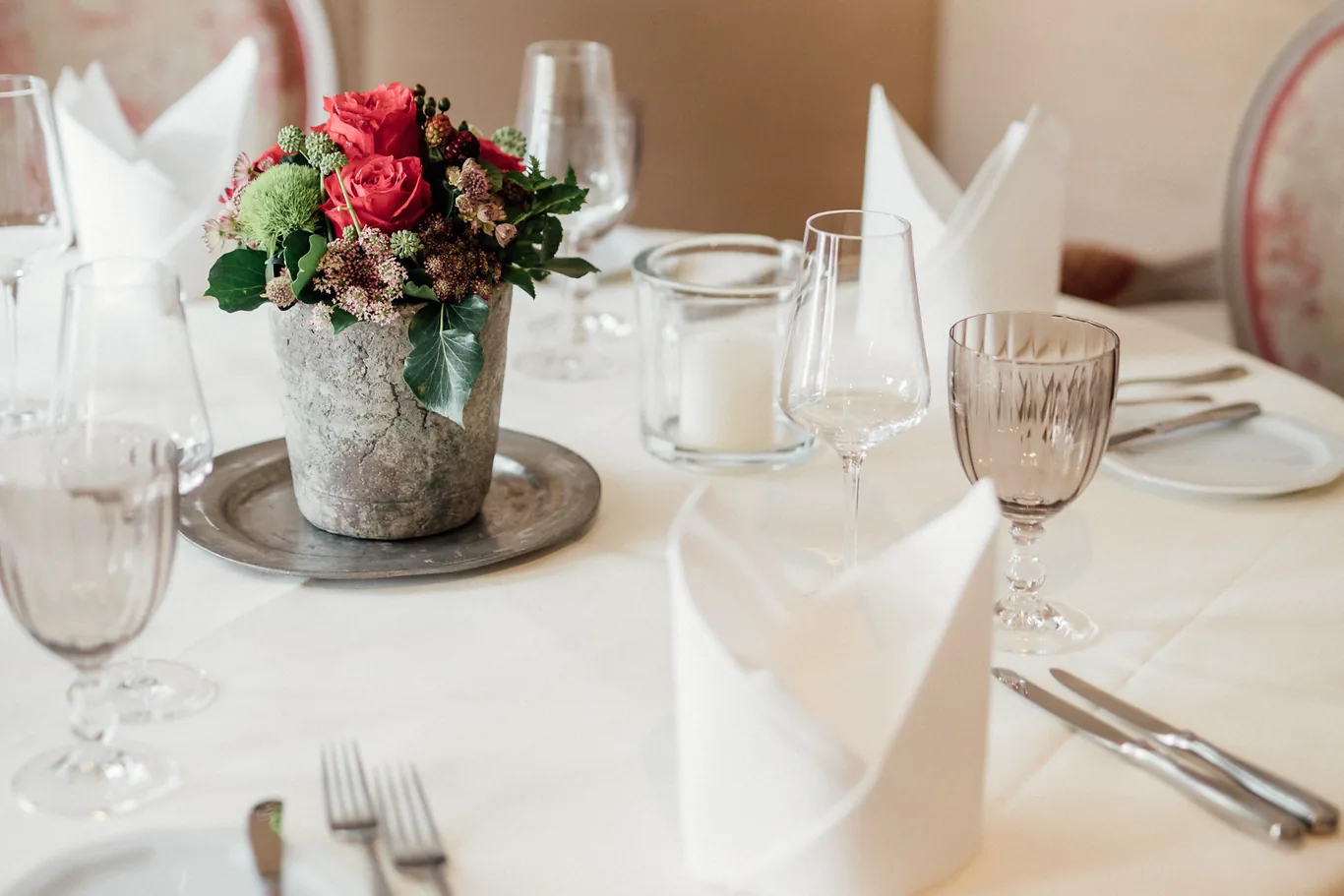 Kleiner gedeckter Tisch mit rosa Blumen und gepolsterten Stühlen im Restaurant des Hotel Krone