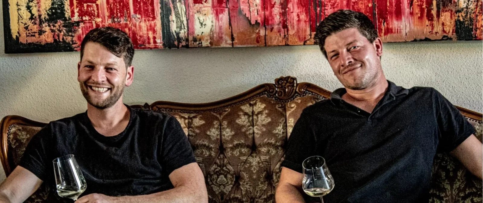 Philipp und Johannes Reibold mit Weingläsern auf einem Sofa